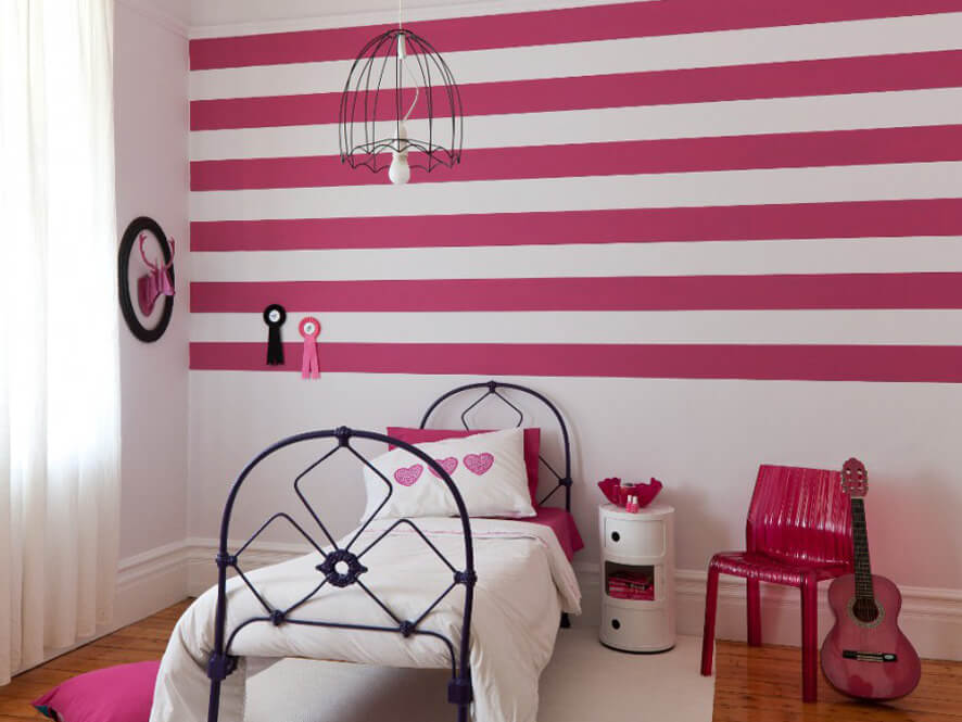 little_kids_pink_striped_feature_wall_bedroom_black_bed_frame_pink_chair_white_rug_timber_floor